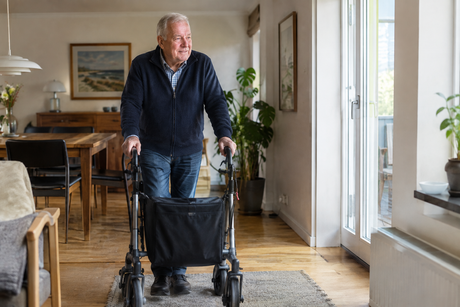 Ældre mand går med rollator i et lyst og hjemligt miljø